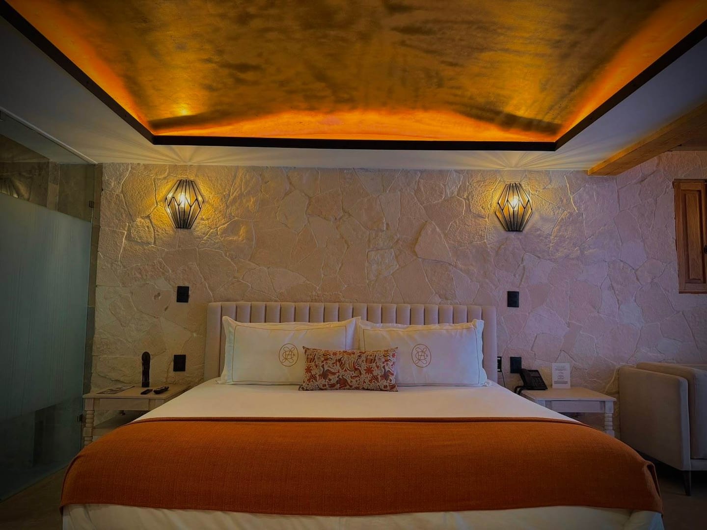 Madera king suite with monogrammed linens, stone wall, and a glowing gold-leaf ceiling