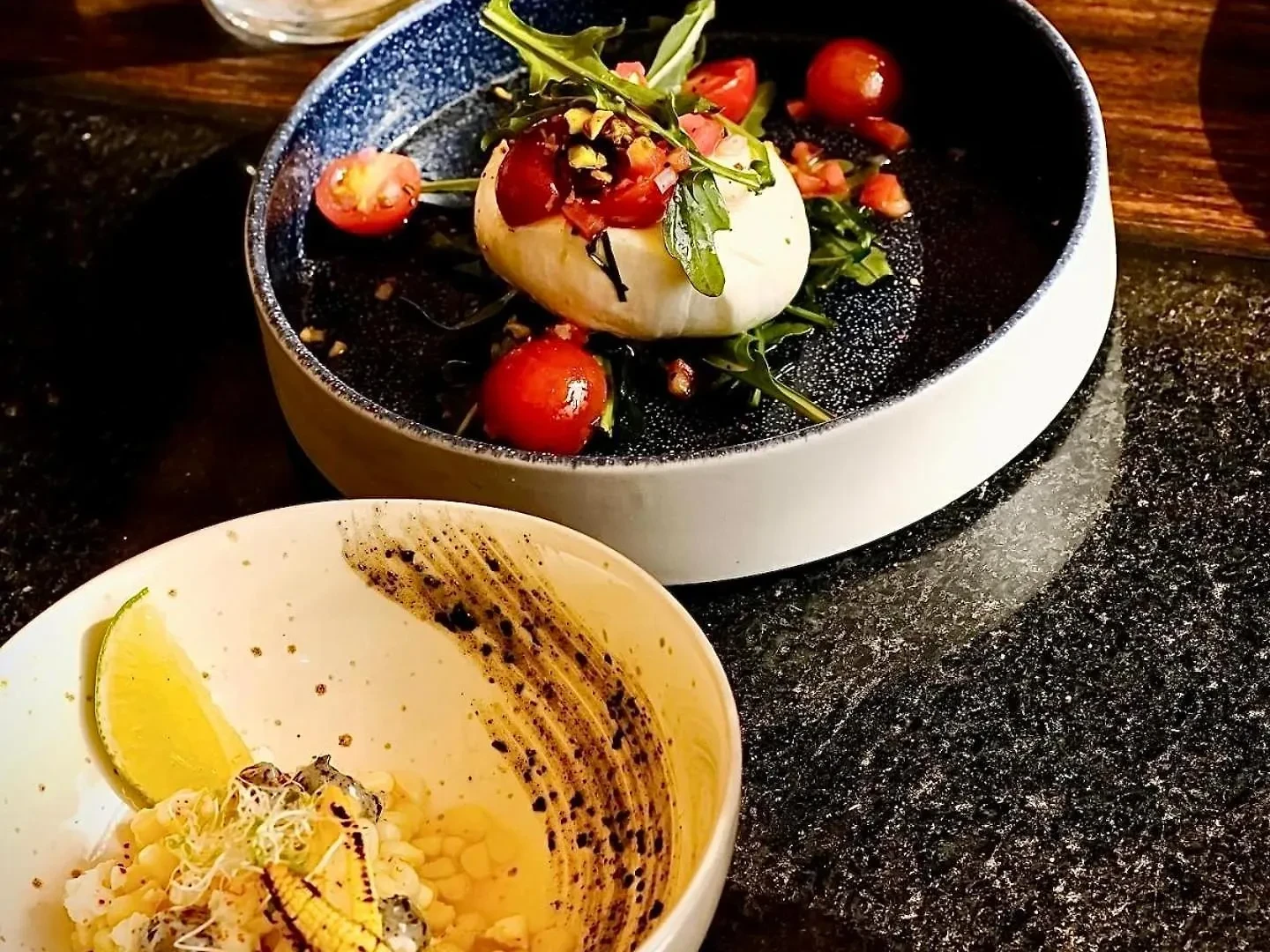 Burrata with arugula and cherry tomatoes beside a charred elote bowl