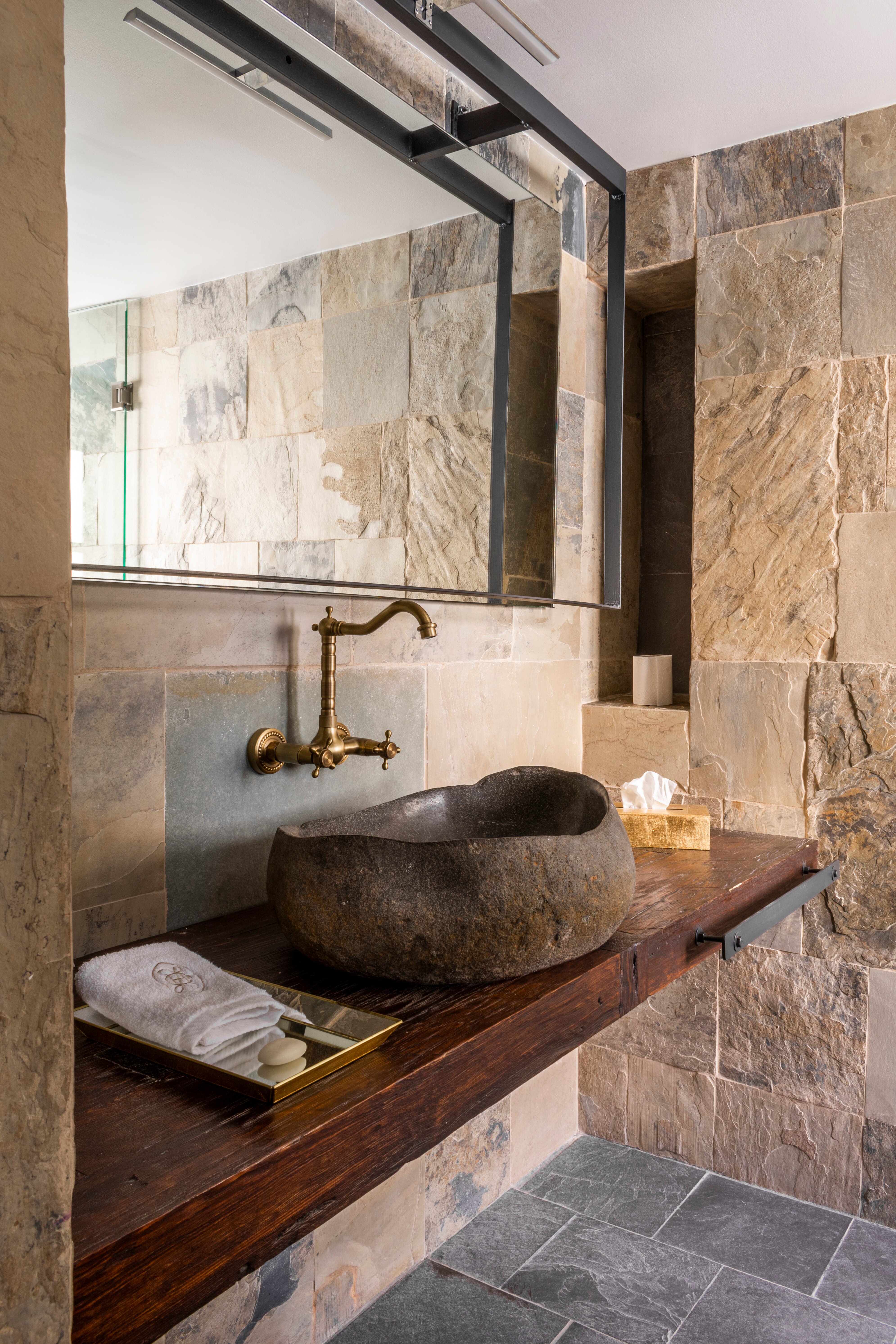 Stone bathroom with carved vessel sink and brass fixtures
