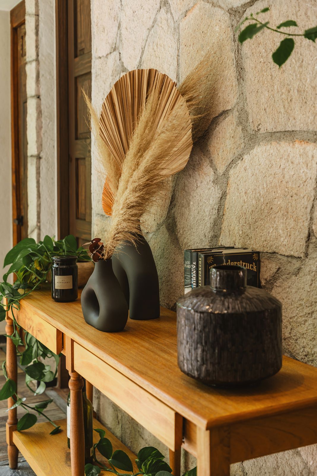 A console table against a stone wall with ceramic vases and a dried palm frond