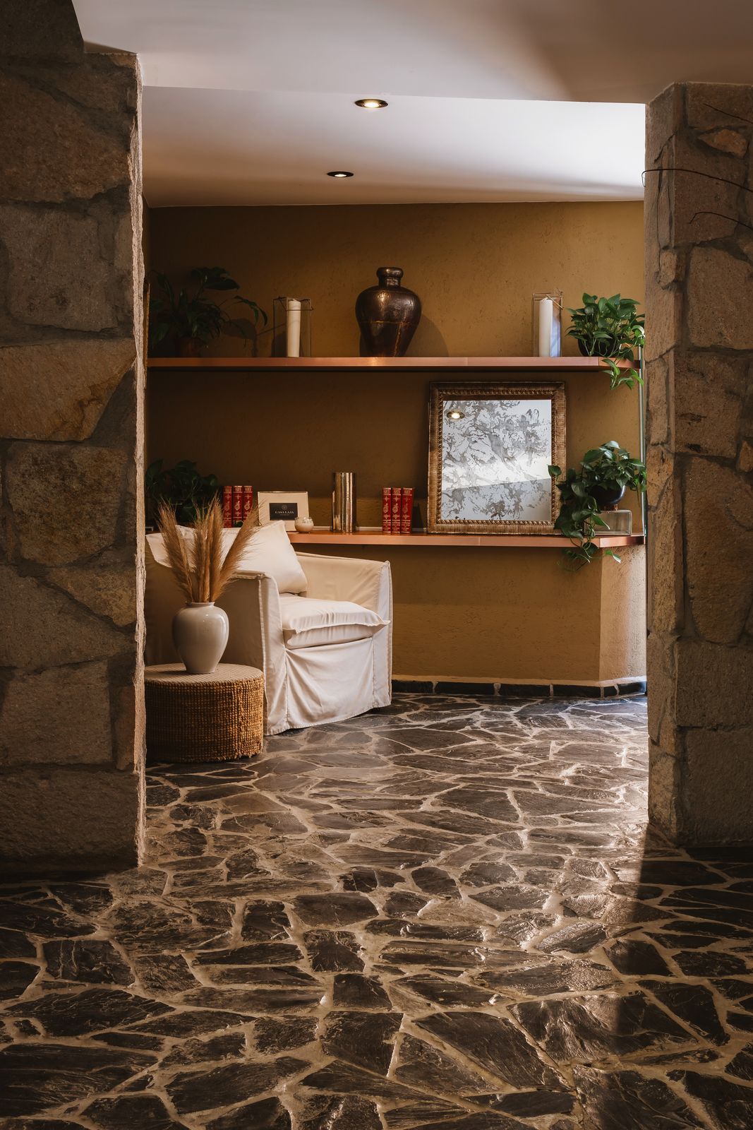 A stone-floored passage opening into the lounge, with an armchair and a shelf of ceramics