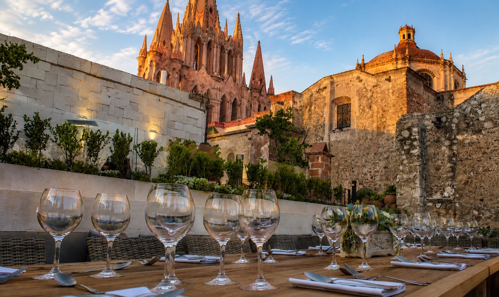A long table set with wine glasses on the Quince rooftop at golden hour, the Parroquia glowing behind