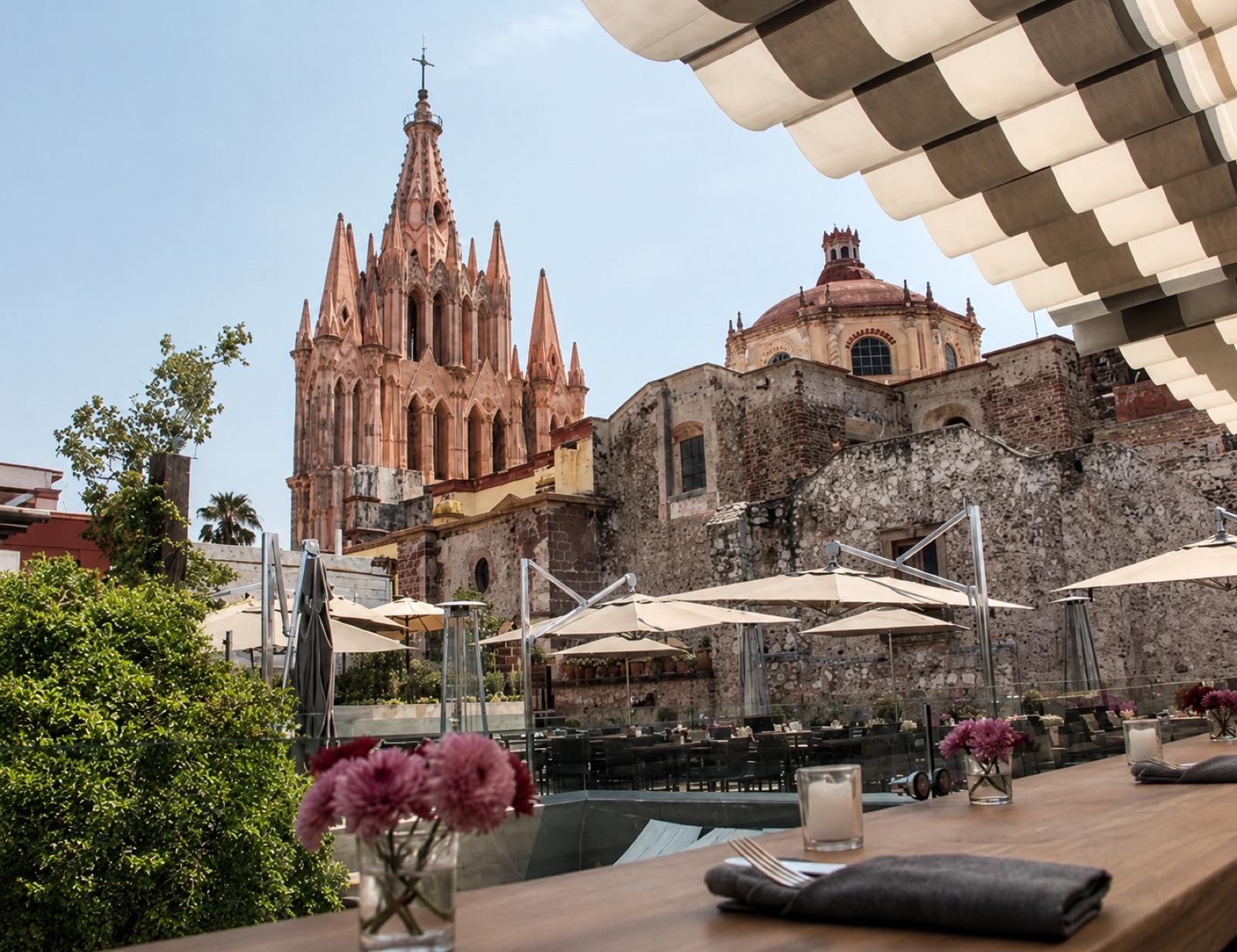 Tables under umbrellas on the Quince rooftop restaurant with the Parroquia and the dome of Las Monjas rising behind