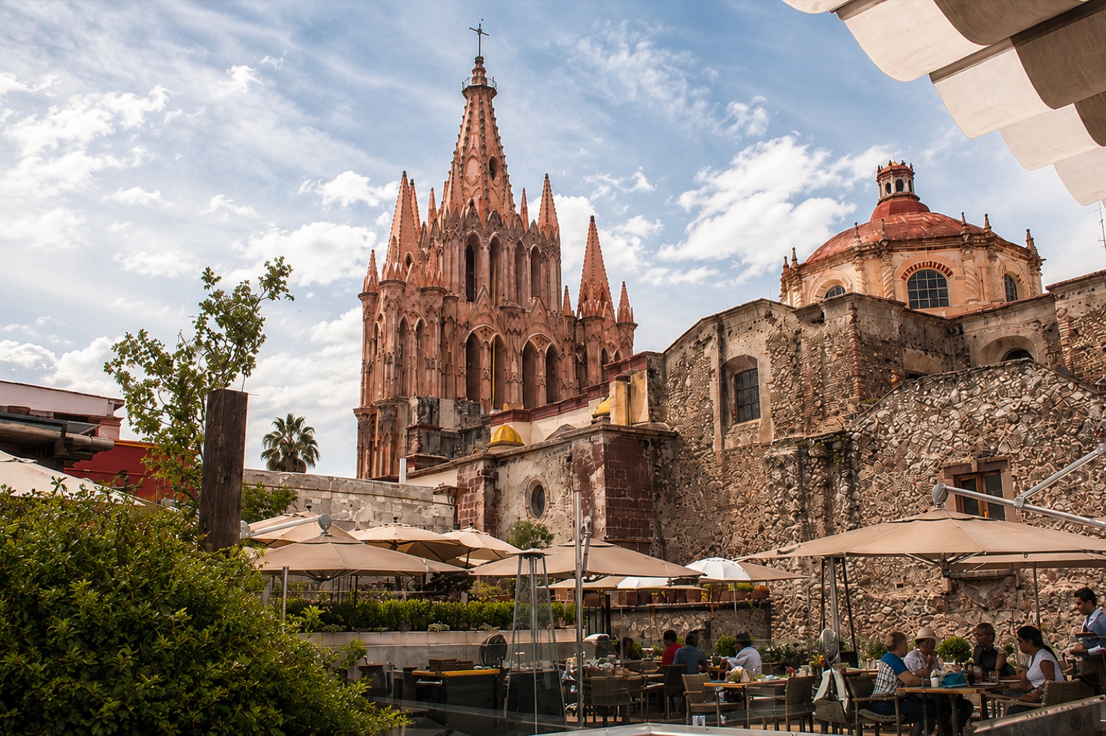 Daytime dining under umbrellas on the Quince rooftop terrace with the Parroquia and a stone dome in view