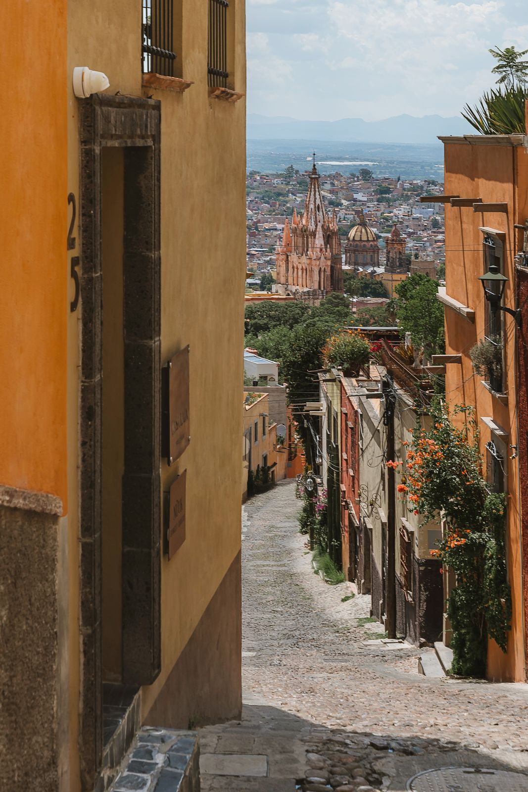 A cobblestone street falling away toward the spires of the Parroquia